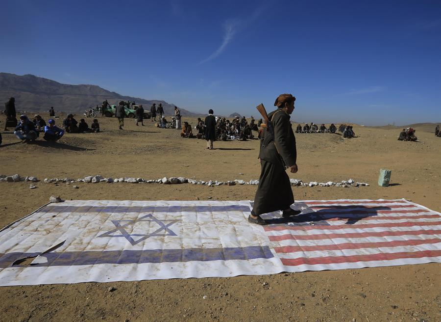 Un integrante de una tribu leal a los hutíes camina encima de las banderas de Israel y Estados Unidos durante un encuentro para combatientes recientemente reclutados el 22 de enero en las afueras de Saná. EFE/YAHYA ARHAB