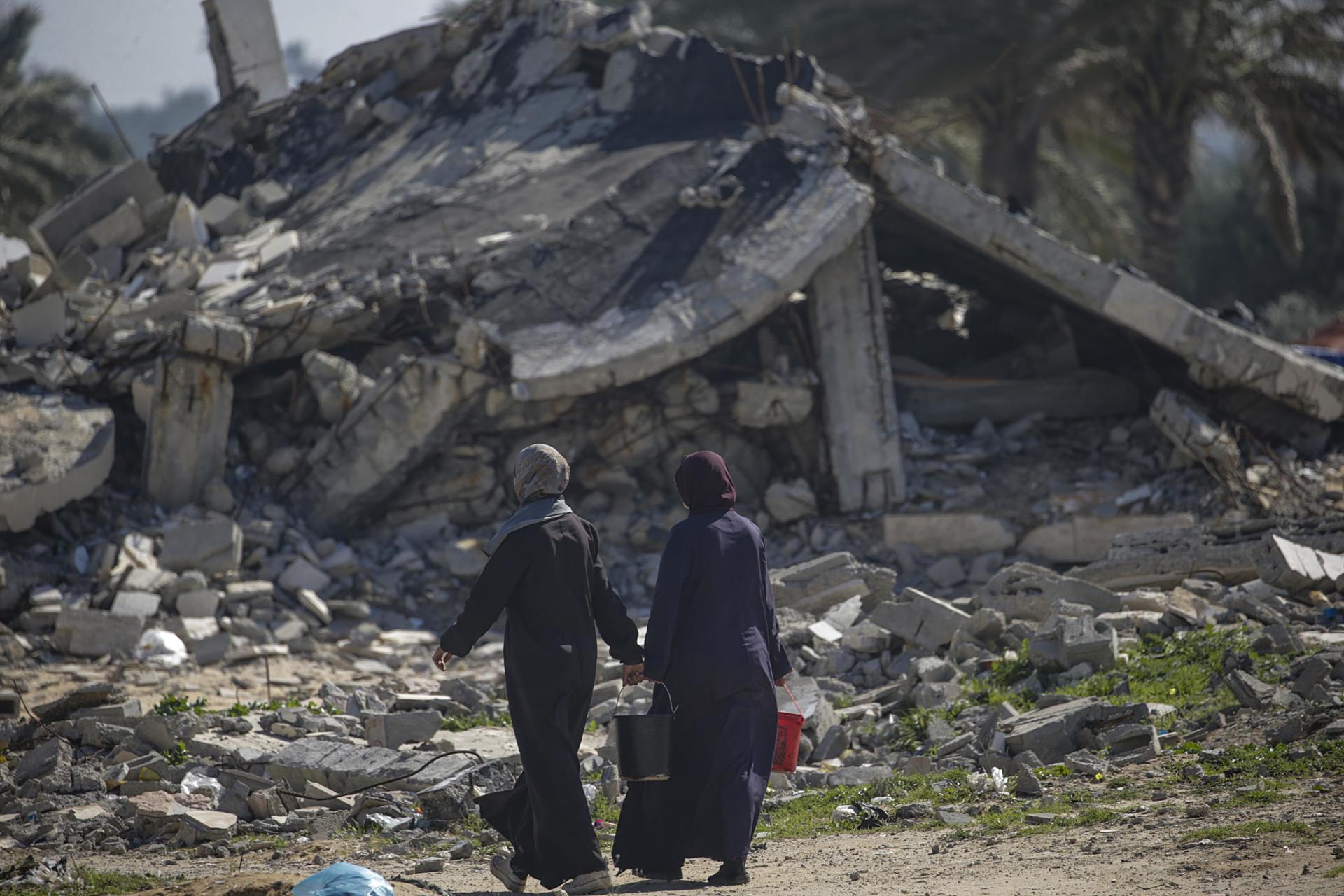 Mujeres palestinas desplazadas pasan junto a un edificio destruido en Deir Al Balah, en el sur de la Franja de Gaza, el 14 de febrero de 2024. EFE/EPA/MOHAMMED SABLE
