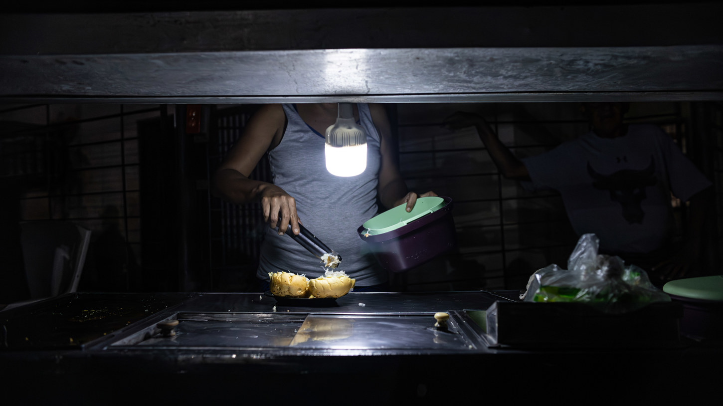 Una persona vende comida ayudado con un bombillo en medio de la oscuridad durante un corte eléctrico, el 29 de febrero de 2024 en Maracaibo (Venezuela). (Foto de Henry Chirinos de la agencia EFE)