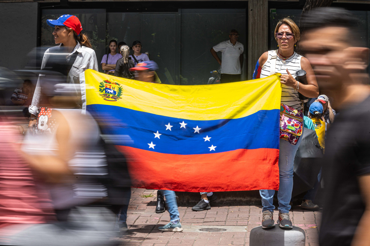 Dos mujeres sostienen una bandera de Venezuela durante una concentración convocada por la líder opositora María Corina Machado y el abanderado de la oposición, Edmundo González Urrutia, en Caracas (Venezuela). (Fotografía Henry Chirinos de la agencia EFE)