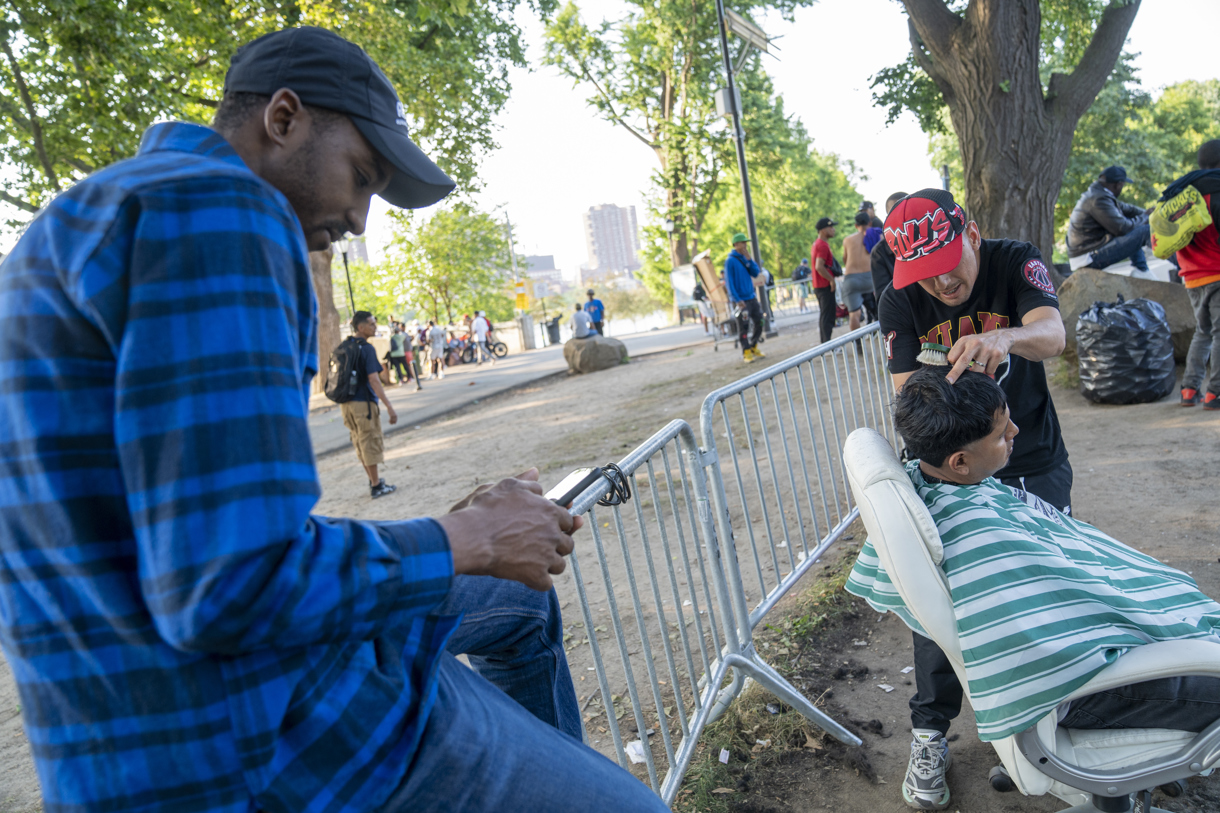 Fotografía que muestra un inmigrante mientras le corta el cabello a otro afuera del refugio de Randall Island en Nueva York (EUA). (Foto de Ángel Colmenares de la agencia EFE)