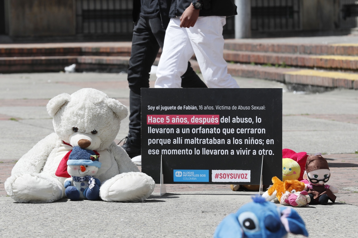 Fotografía de archivo de varios juguetes junto a un cartel de protesta que resume una historia de abuso a un niño, durante un plantón en la Plaza del céntrico barrio 20 de Julio, en Bogotá (Colombia). (Foto de Carlos Ortega de la agencia EFE)