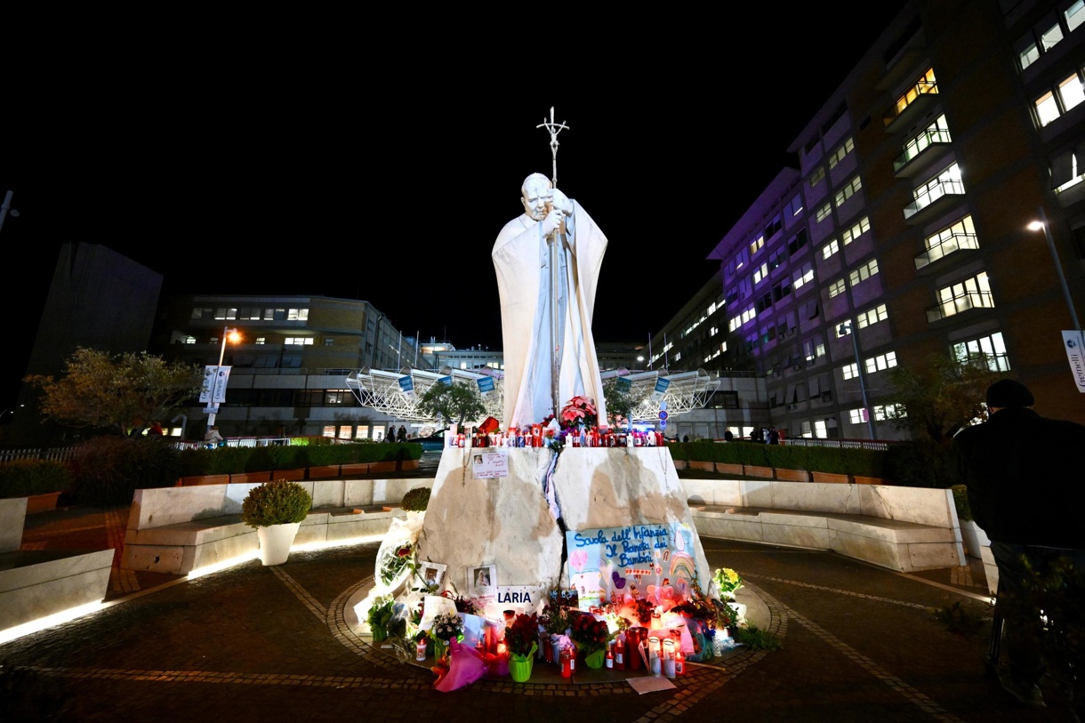 Flores y velas se encuentran a los pies de una estatua del Papa San Juan Pablo II fuera del Hospital Gemelli en Roma, Italia, 27 de febrero de 2025, donde el Papa Francisco está hospitalizado para pruebas y tratamiento por bronquitis. (Foto de Alessandro Di Meo de la agencia EFE/EPA)