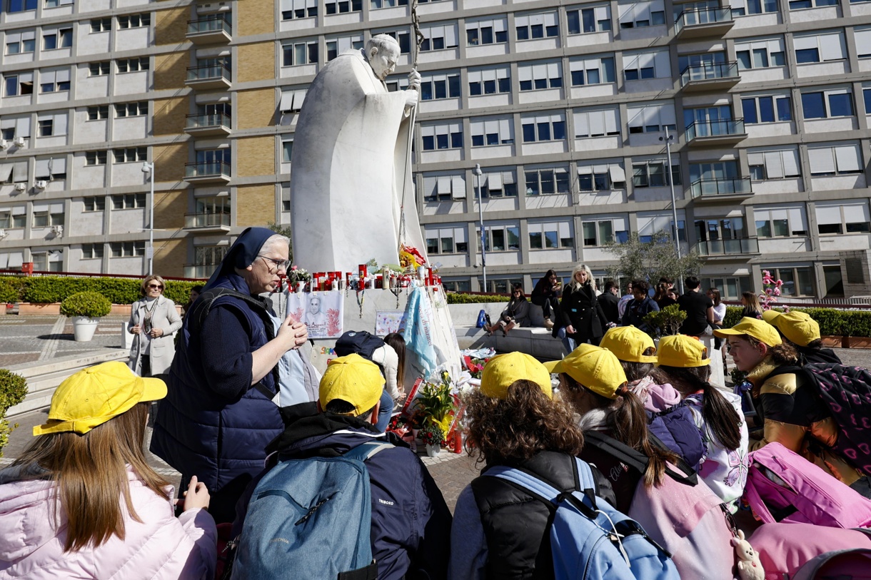 Niños de una escuela primaria en Rivoli, cerca de Turín, oran frente a la estatua de Juan Pablo II en la entrada del Hospital Gemelli, donde está hospitalizado el Papa Francisco, en Roma, Italia, 18 de marzo de 2025. (Foto de Fabio Frustaci de la agencia EFE/EPA)