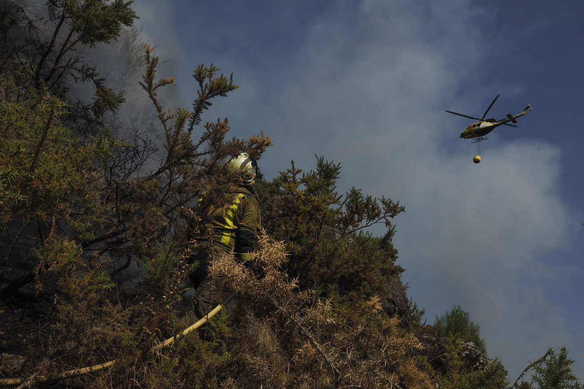 Un helicóptero de la lucha contra el fuego vuela sobre un bombero que trabaja en la extinción del incendio de la parroquia de A Cova (Lugo, Galicia). (Foto de Eliseo Trigo de la agencia EFE)