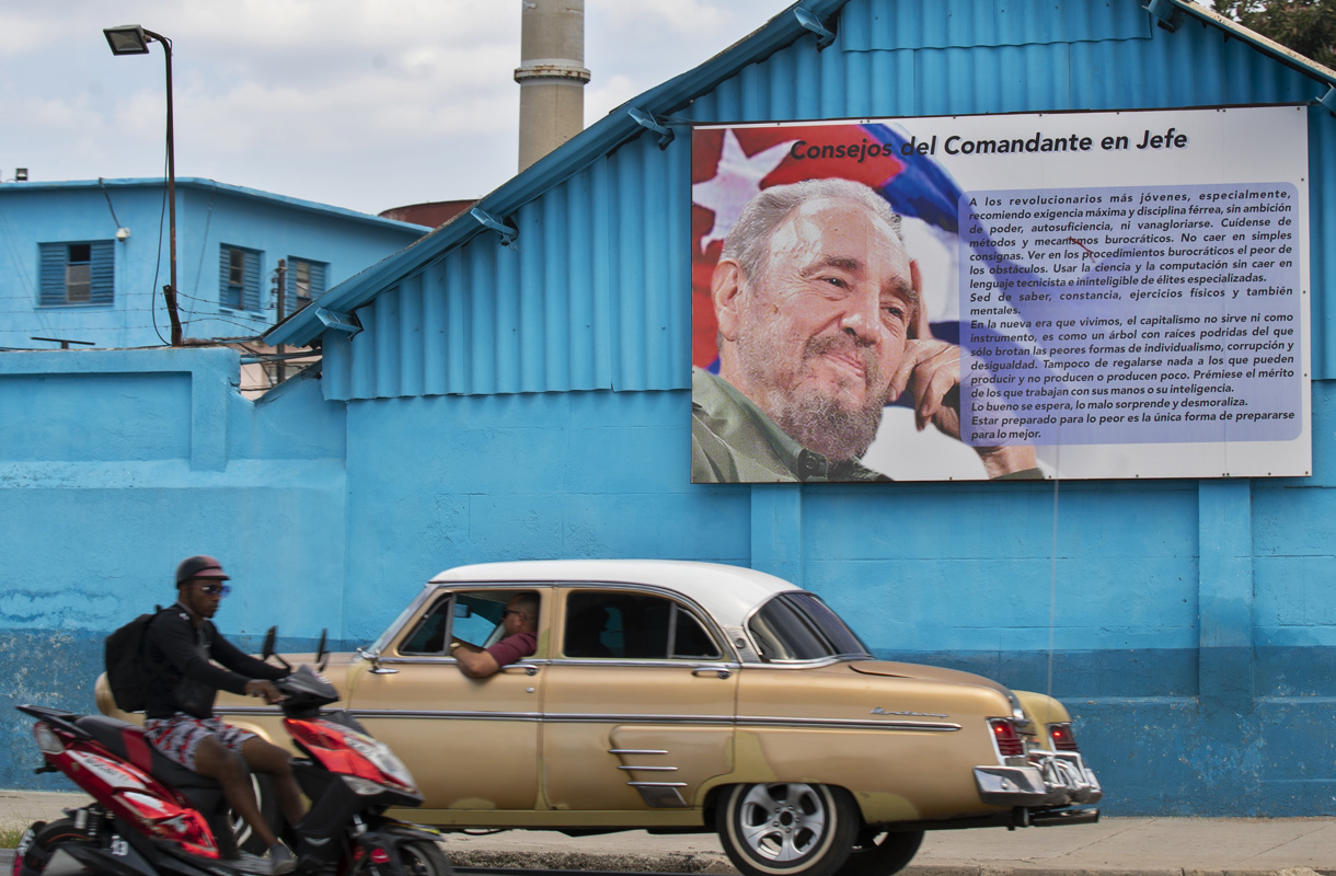Un auto clásico y una motocicleta que pasan frente a una valla con un retrato de Fidel Castro, en La Habana (Cuba). (Foto de archivo de Yander Zamora de la agencia EFE)