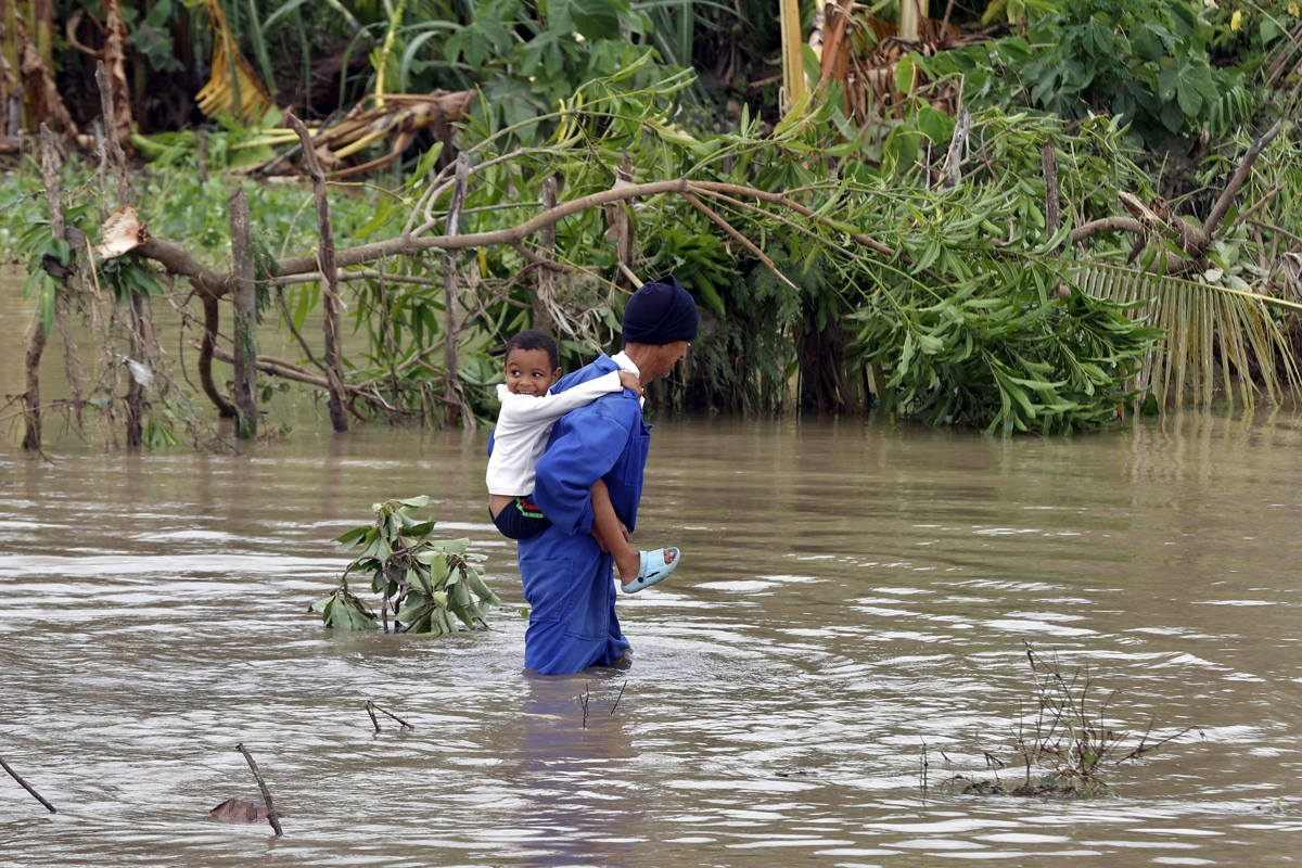 Un hombre cruzando un río crecido mientras carga a un niño, en el poblado de Guama en Santiago de Cuba (Cuba). (Foto del 29 de octubre de 2025 de Ernesto Mastrascusa de la agencia EFE)