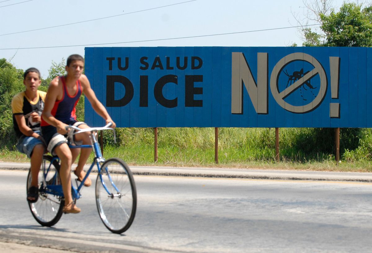 Dos jóvenes pasando frente a un cartel sobre el dengue en Cuba. (Foto de archivo de Orlando Barría de la agencia EFE)