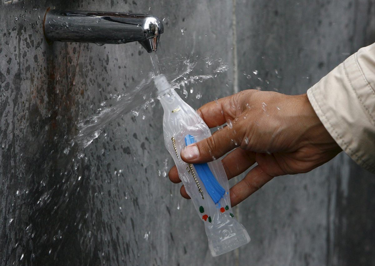 En la imagen de archivo, un peregrino llena de agua una botella con la forma de la Virgen María en una fuente de la gruta del santuario de Lourdes, Francia. (Foto de Guillaume Horcajuelo de la agencia EFE)