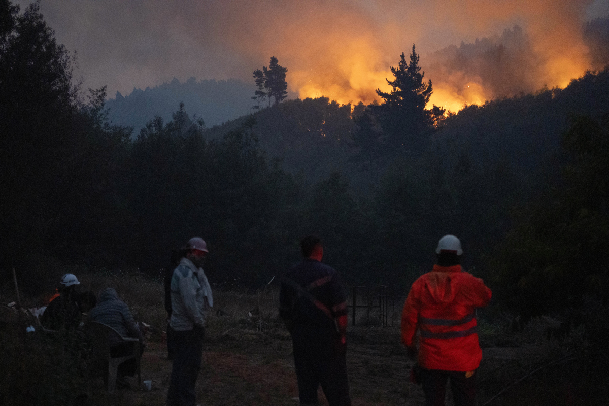 Personas observan un incendio forestal este lunes, en la comuna de Chaimávida, en Concepción a unos 491 km aproximadamente de Santiago (Chile). (Foto de Adriana Thomasa de la agencia EFE)