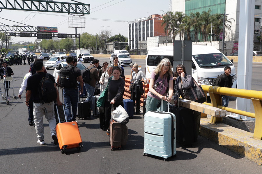 Pasajeros caminan ante un bloque de taxistas para llegar a la Terminal 1 del Aeropuerto Internacional de la Ciudad de México. (Foto de EFE)