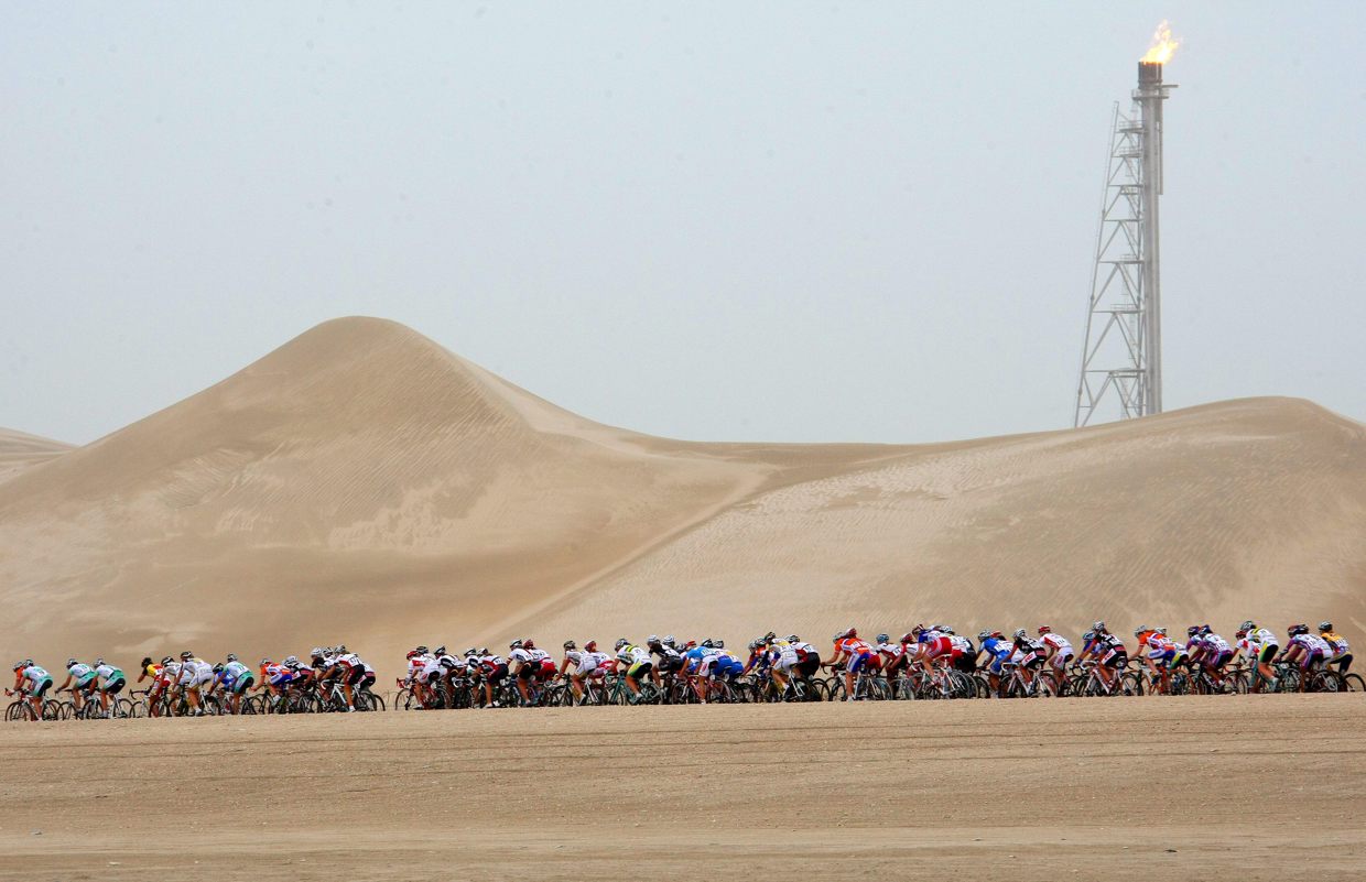 Pelotón de ciclistas pasa junto a una fábrica de gas en el desierto. (Fotografía de archivo de Ian Langsdon de la agencia EFE)